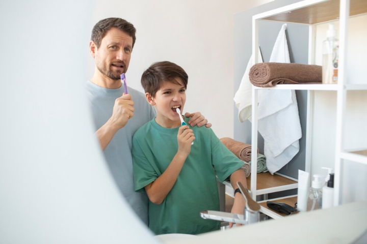 Como se usa el hilo dental: padre e hijo cepillándose los dientes cuidando su higiene bucal